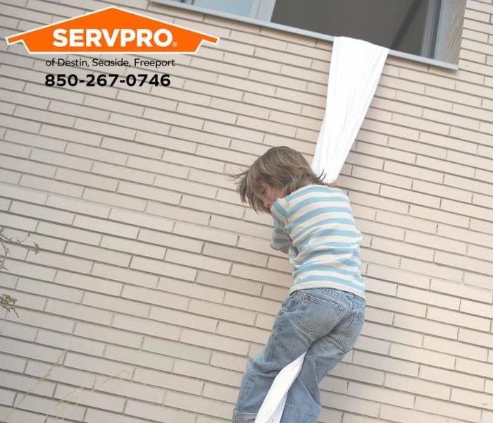A child is climbing out of a window using s sheet rope. 