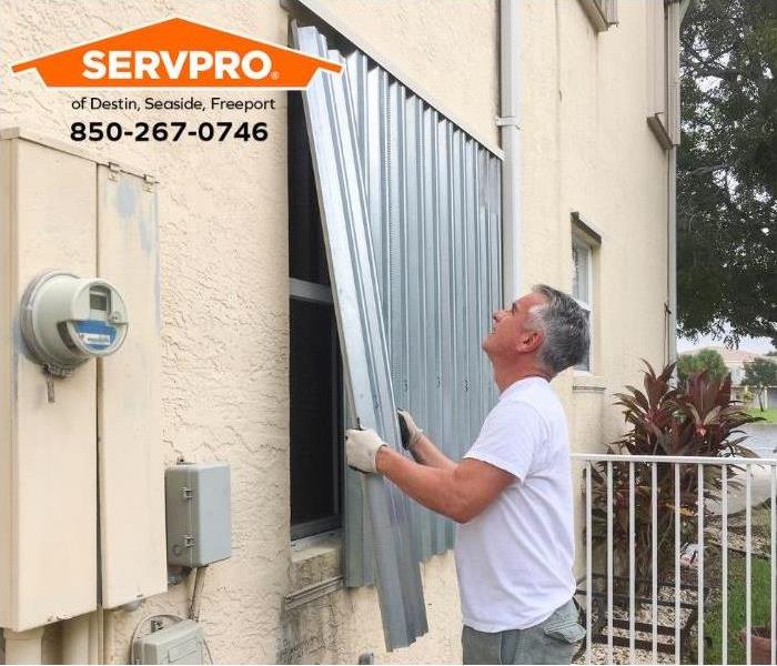 A person is installing storm shutters over a window. 